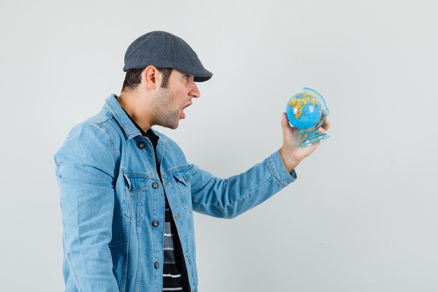 Jeune homme en veste, casquette regardant globe et à la surprise.