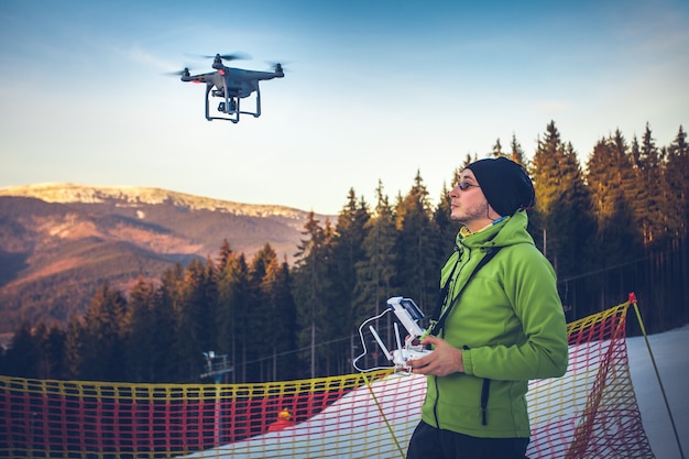 Jeune homme en veste verte actionnant un drone à l'aide d'une station de ski télécommandée en arrière-plan