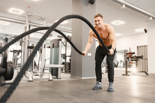 Photo gratuite jeune homme en vêtements de sport faisant des exercices avec une corde spéciale au gymnase