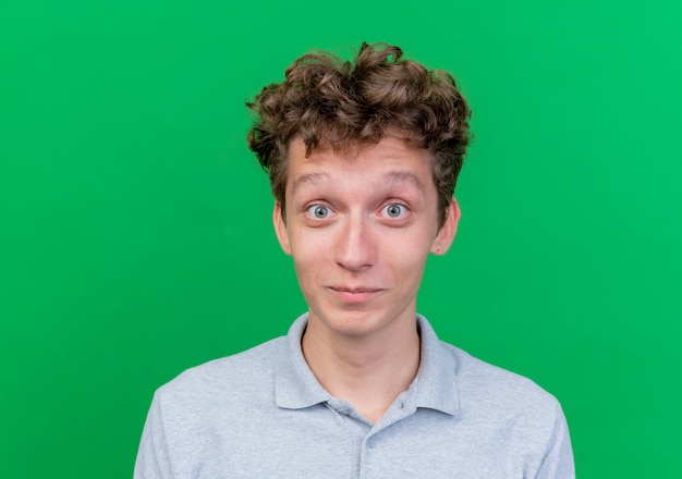 Jeune homme vêtu d'un polo gris aux yeux grands ouverts heureux et positif sur vert