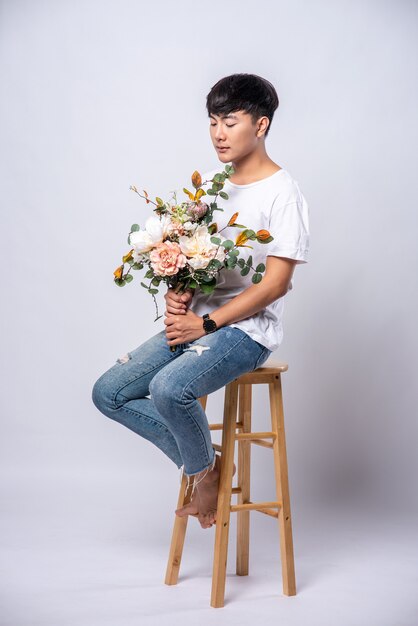 Un jeune homme vêtu d'un t-shirt blanc est assis sur une chaise haute et tient des fleurs.