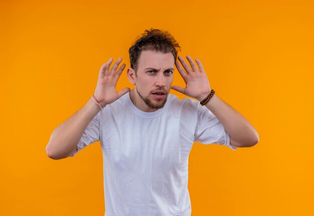 Jeune homme vêtu d'un t-shirt blanc a mis ses mains autour des oreilles sur un mur orange isolé