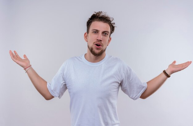 Jeune homme vêtu d'un t-shirt blanc se propage les mains sur un mur blanc isolé