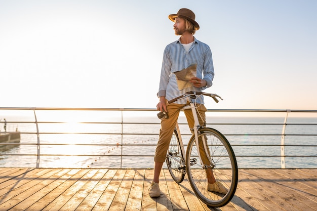 Jeune homme voyageant à vélo au bord de la mer en vacances d'été au bord de la mer au coucher du soleil, tenant une carte touristique avec appareil photo