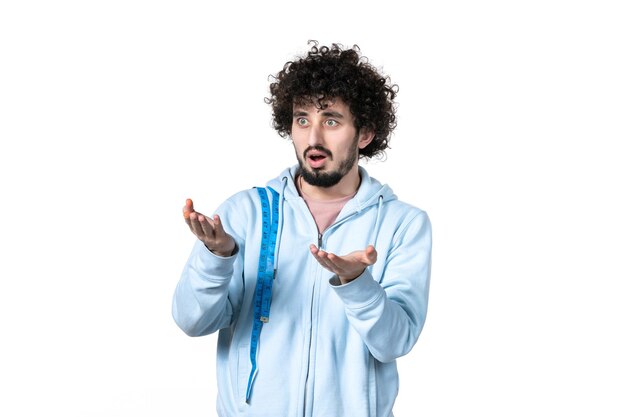 Jeune homme vue de face avec un ruban à mesurer sur une surface blanche