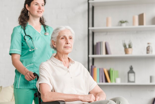 Jeune infirmière aidant désactivé senior femme assise sur une chaise roulante