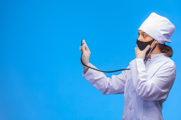 Jeune infirmière en masque noir vérifie le patient avec un stéthoscope.