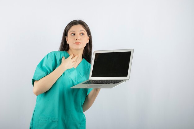 Jeune infirmière posant avec ordinateur portable sur blanc.