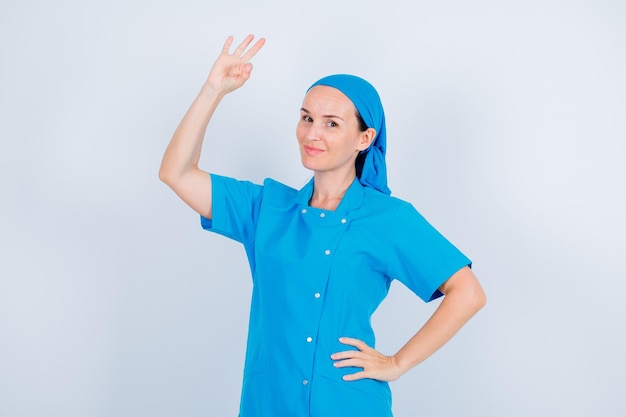 Jeune infirmière pose devant la caméra en montrant un geste correct et en mettant l'autre main sur la taille sur fond blanc