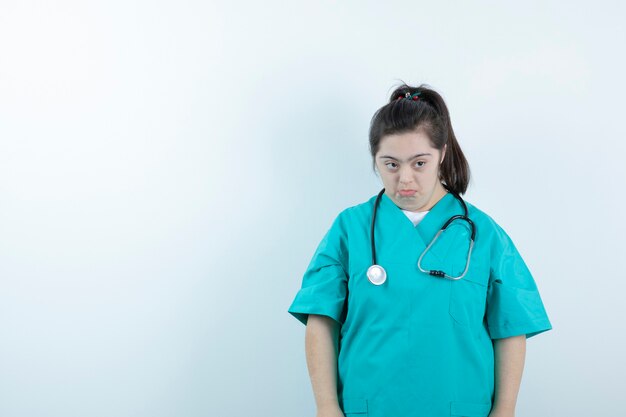 Jeune infirmière avec stéthoscope posant contre un mur blanc.