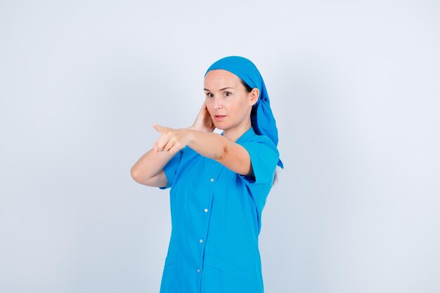 Une jeune infirmière surprise pointe du doigt avec l'index sur fond blanc