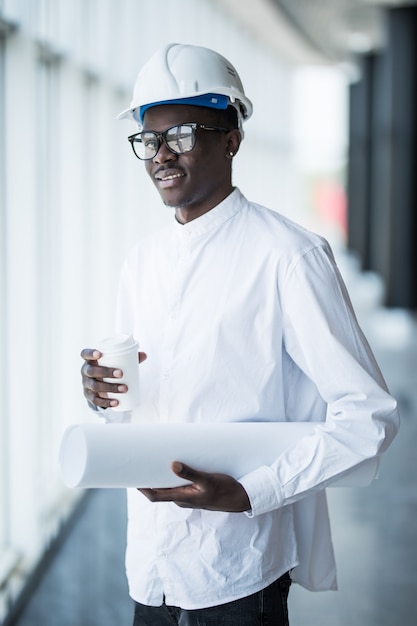 Photo gratuite jeune ingénieur afro-américain avec des imprimés bleus devant des fenêtres panoramiques au bureau