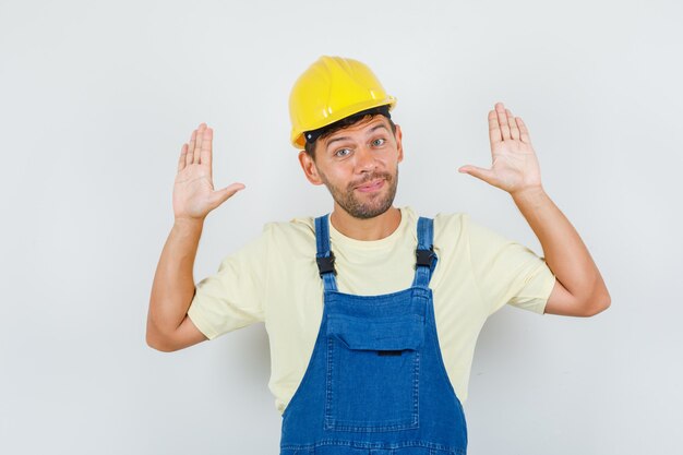 Jeune ingénieur montrant des paumes en geste de reddition en uniforme et à la vue de face, joyeuse.