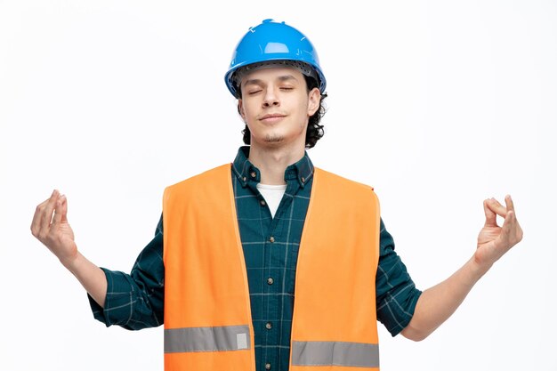 Jeune ingénieur pacifique portant un casque de sécurité et un gilet de sécurité méditant les yeux fermés isolés sur fond blanc