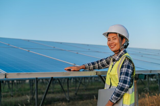 Jeune ingénieure inspectrice asiatique touchant à la vérification du fonctionnement du panneau solaire photovoltaïque dans une station extérieure tenant un ordinateur portable et regardant la caméra avec un espace de copie de sourire