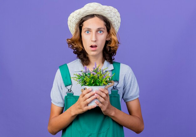 Jeune jardinier homme portant combinaison et chapeau tenant une plante en pot