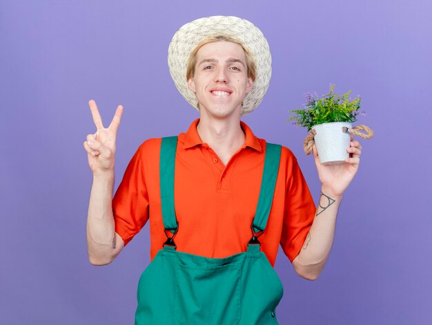 Jeune, jardinier, homme, porter, combinaison, et, chapeau, tenue, plante pot, sourire