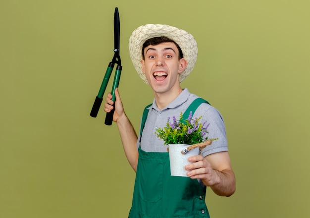 Un jeune jardinier joyeux portant un chapeau de jardinage tient une tondeuse et un pot de fleurs