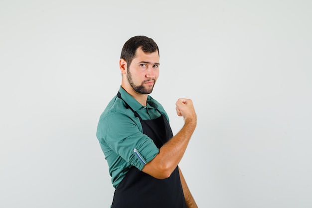 Jeune jardinier montrant son muscle du bras en t-shirt, tablier et semblant puissant. vue de face.