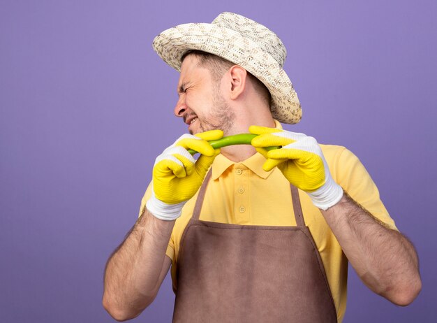 Jeune Jardinier Portant Combinaison Et Chapeau Dans Des Gants De Travail Tenant Le Piment Vert Tournant La Tête Contre Le Poivre Debout Sur Le Mur Violet