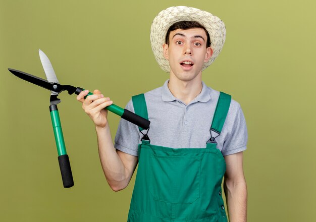 Un jeune jardinier surpris portant un chapeau de jardinage détient des tondeuses