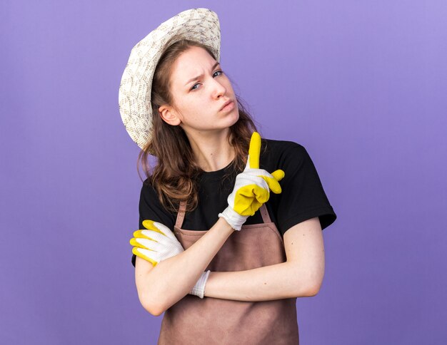 Jeune jardinière confiante portant un chapeau de jardinage avec des gants montrant un isolé sur un mur bleu