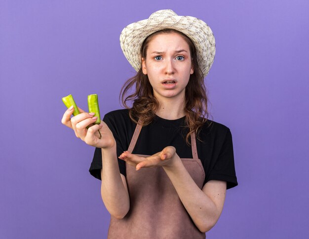 Jeune jardinière confuse portant un chapeau de jardinage tenant du poivre cassé