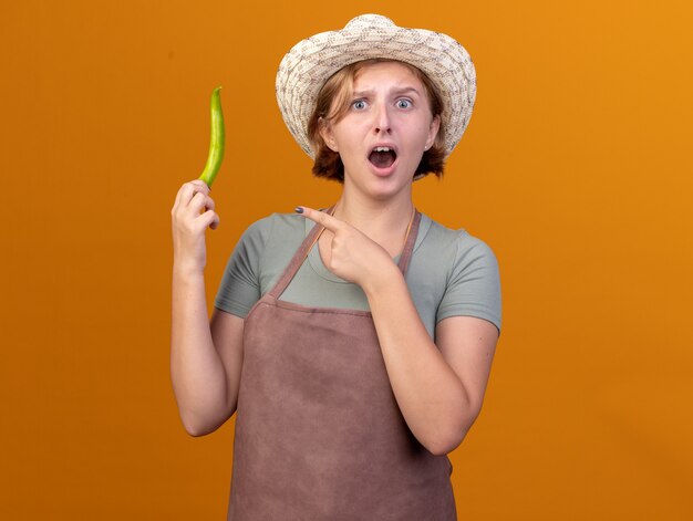 Jeune jardinière slave anxieuse portant un chapeau de jardinage tenant et pointant du doigt le piment