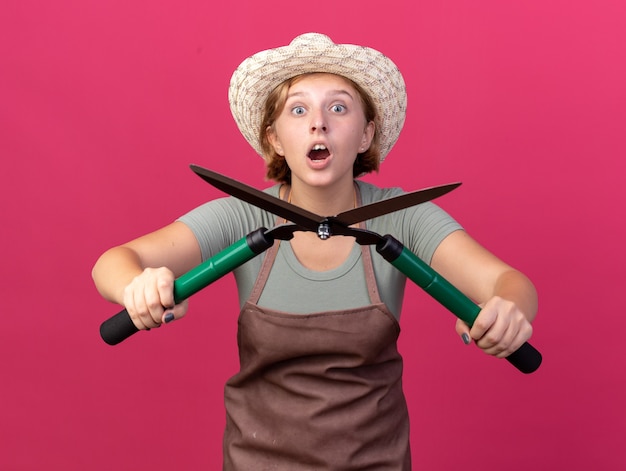 Photo gratuite jeune jardinière slave excitée portant un chapeau de jardinage et des gants tenant des ciseaux de jardinage isolés sur un mur rose avec espace pour copie