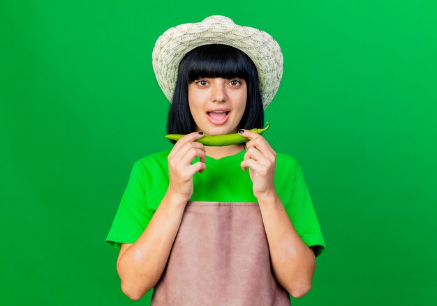 Jeune jardinière surprise en uniforme portant un chapeau de jardinage détient du piment