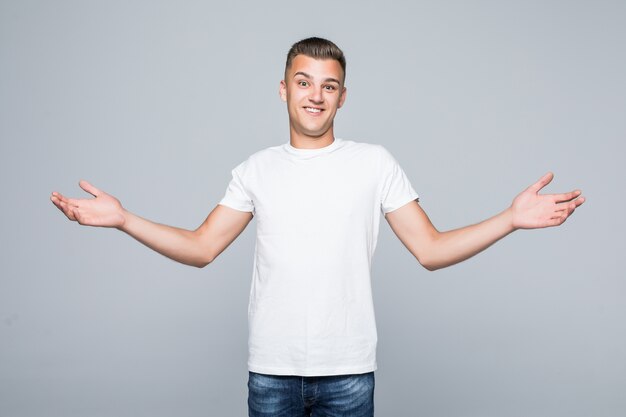 Jeune joli homme dans un T-shirt blanc isolé sur blanc tenir les bras des deux côtés