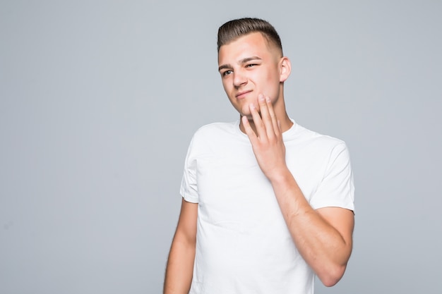 Jeune joli homme dans un T-shirt blanc isolé sur blanc touche son visage