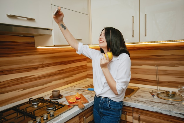 Jeune et jolie brune debout dans la cuisine avec téléphone