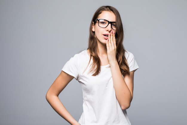 Jeune jolie dame timide à lunettes en t-shirt blanc et blue-jeans rester devant fond blanc studio