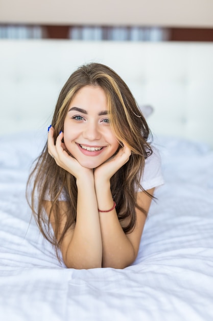 Jeune jolie femme allongée au bout du lit souriante, la tête appuyée sur sa main.