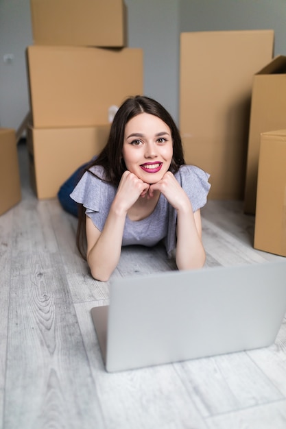 Une jeune et jolie femme asiatique parlant au téléphone et utilisant son ordinateur portable dans sa nouvelle maison