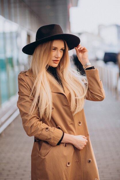 Jeune jolie femme au chapeau noir et manteau beige marchant par mall