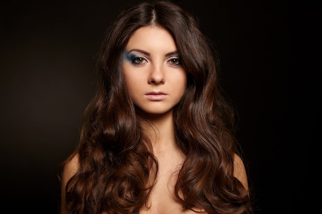 Jeune jolie femme aux longs cheveux noirs maquillage lumineux isolé sur fond noir
