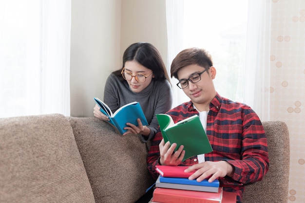 Jeune jolie femme et beau petit ami portant des lunettes et assis à la lecture de livres sur un canapé à la maison