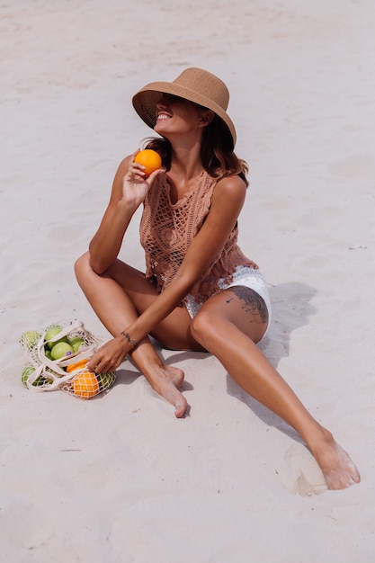 Jeune jolie femme bronzée caucasienne en vêtements tricotés et chapeau sur la plage