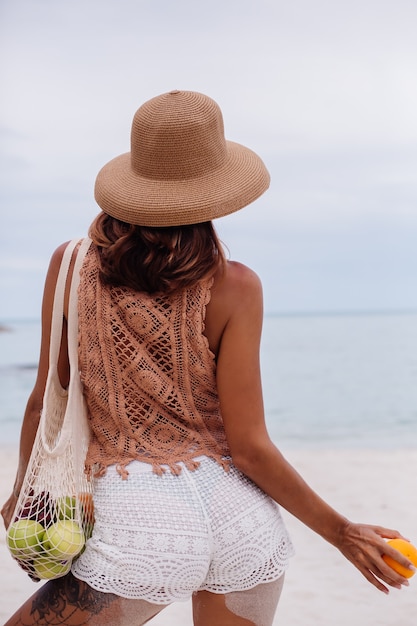 Jeune jolie femme bronzée caucasienne en vêtements tricotés et chapeau sur la plage