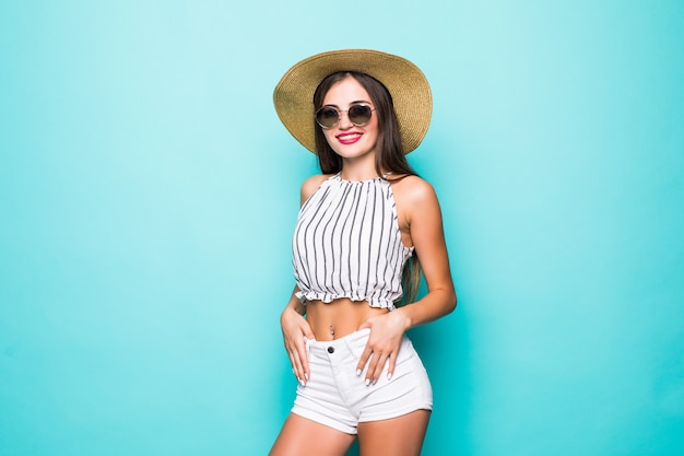 Jeune jolie femme en chapeau de vêtements d'été et lunettes de soleil sur fond turquoise