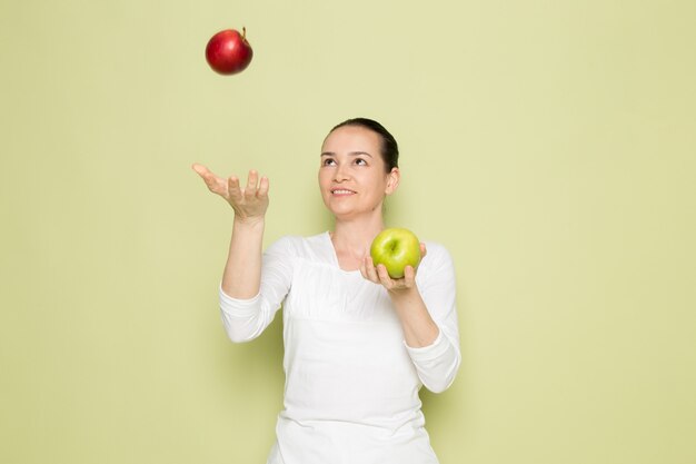 Jeune jolie femme en chemise blanche, souriant et jouant avec des pommes vertes et rouges