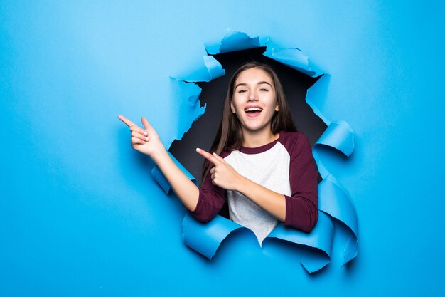 Jeune jolie femme côté pointu tout en regardant à travers le trou bleu dans le mur de papier.