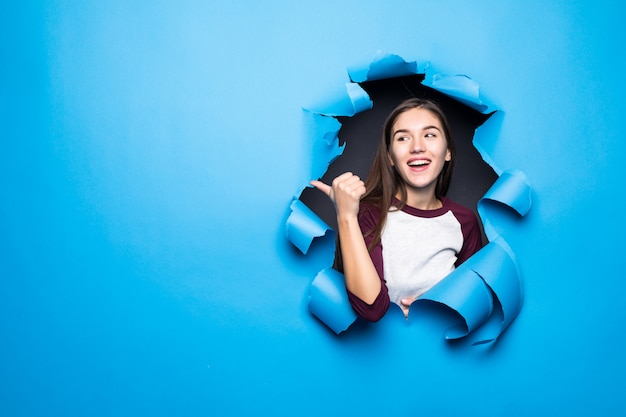 Jeune jolie femme côté pointu tout en regardant à travers le trou bleu dans le mur de papier.