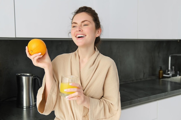 Jeune jolie femme cuisinant à la maison cuisine du matin nourriture saine buvant du jus d'orange