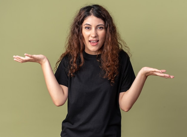 Jeune jolie femme désemparée regardant devant montrant les mains vides isolées sur un mur vert olive