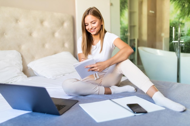 Jeune jolie femme étudie avec un ordinateur portable sur le lit