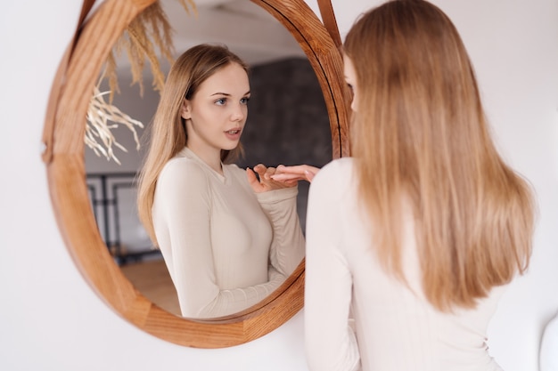 Jeune jolie femme à la maison se regarde dans le miroir s'amusant