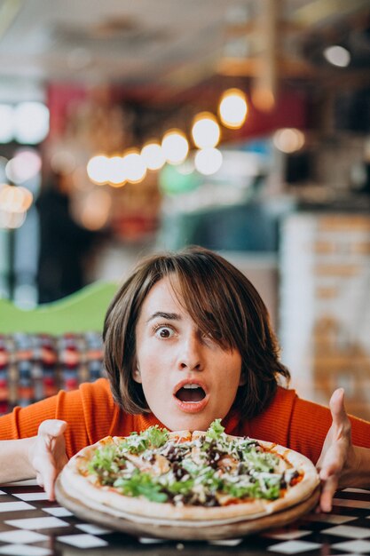 Jeune jolie femme mangeant une pizza au bar à pizza